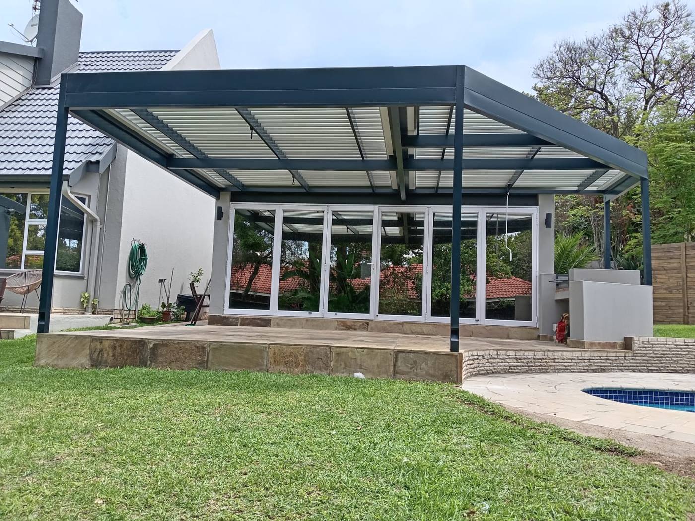 Charcoal louvre with white blades over a raised sandstone terrace in Lonehill